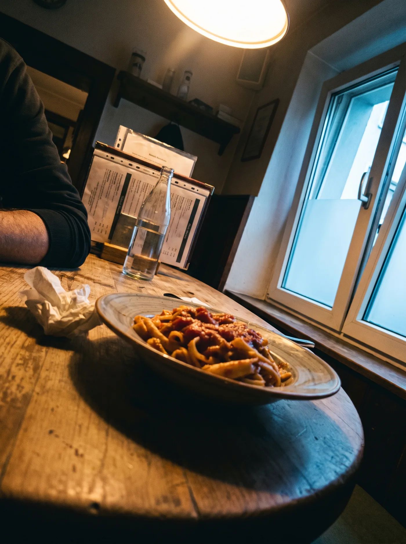 Handyfoto eines Tellers Pasta zwischen zwei Gästen, Deckenlicht